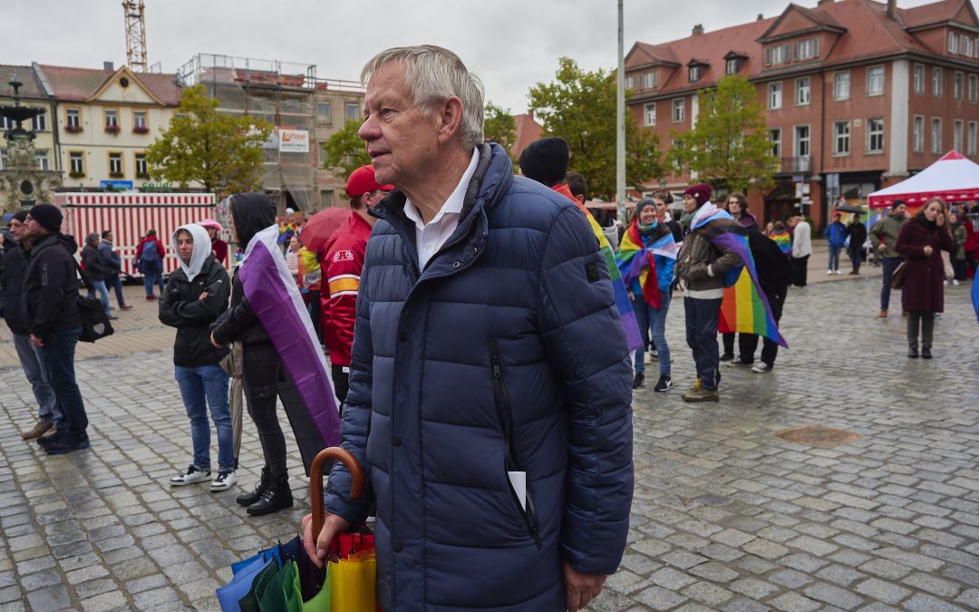 Herr Freller auf dem Schlossplatz in Erlangen mit Regenbogenregenschirm unter den Demontierenden des CSDs 2022.